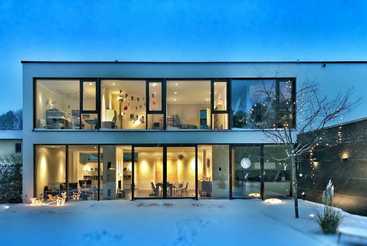 A modern house with large windows and a snow-covered yard on a snow day.